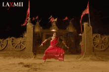 a woman in a red dress is dancing in the dirt in front of a laxmii logo