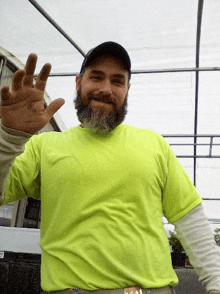 a man with a beard wearing a neon yellow shirt waves his hand