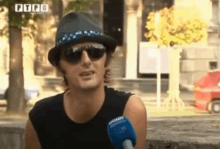 a man wearing a hat and sunglasses talks into a microphone with ptpc written on the bottom