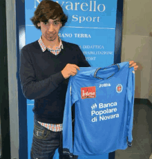 a man is holding a blue jersey that says banca popolare di novara