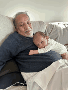 an older man is holding a baby in his arms on a couch