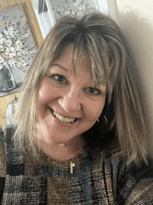 a woman wearing a plaid shirt and a necklace with a cross on it smiles