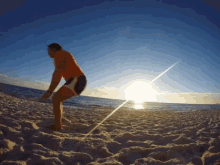 a man in an orange shirt and black shorts stands on a sandy beach