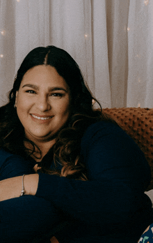 a woman in a blue shirt is smiling while sitting on a brown couch