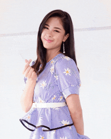 a woman in a blue and white striped dress is making a heart shape with her hand