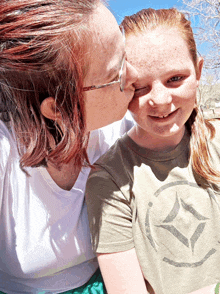 a woman kisses a young girl on the cheek who is wearing a green shirt with a diamond on it