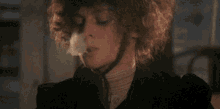 a woman with curly hair is smoking a cigarette and making a cloud of smoke coming out of her mouth .