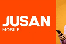 a person holding a cell phone in front of an orange and yellow jusan mobile logo