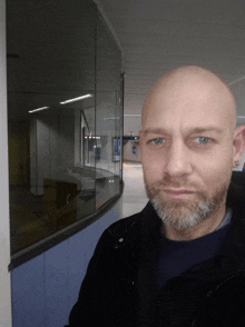 a bald man with a beard stands in front of a window