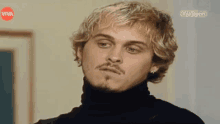 a man with blonde hair and a mustache is wearing a black turtleneck sweater .