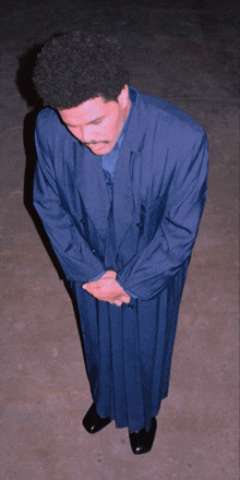 a man in a blue suit stands with his hands folded in prayer