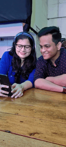 a man and a woman sit at a table looking at a phone