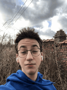 a young man wearing glasses and a blue hoodie poses for a picture