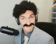 a man in a suit and tie with a fake mustache is standing in front of a microphone