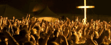 a crowd of people raise their hands in the air in front of a cross