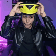 a man in a leather jacket is putting on a yellow helmet