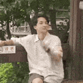 a young man is sitting on a bench in front of a no smoking sign and smoking a cigarette .