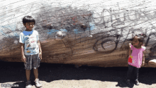 a boy and a girl standing in front of a large log with graffiti on it