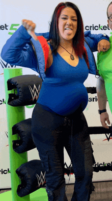 a pregnant woman in a blue shirt and black pants is standing in front of a cricket sign