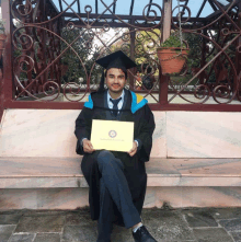 a man in a graduation cap and gown sits on a bench holding a certificate that says bachelor of science