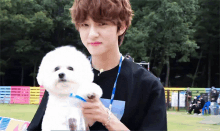 a young man is holding a small white dog in his hands