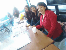 a woman in a red jacket sits at a table with two women