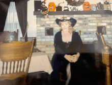 a woman in a witch costume sits in front of a fireplace decorated for halloween