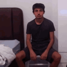 a young man in a black shirt sits on a chair in front of a bed