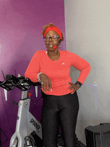 a woman wearing a headband stands next to a spinner bike