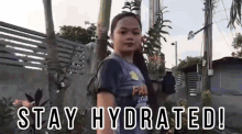 a young girl is standing in front of a fence and a sign that says `` stay hydrated '' .