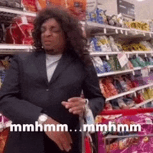 a man in a suit is standing in a grocery store with a cart .