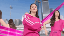 a woman in a pink off the shoulder top is dancing in front of a city .