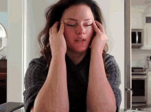 a woman with her eyes closed holds her hands to her head