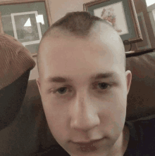 a man with a shaved head is sitting on a couch in front of framed pictures