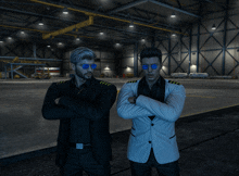 two men standing next to each other with their arms crossed in a hangar