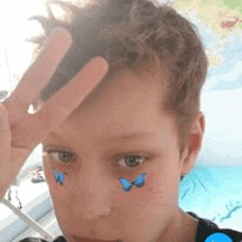 a young boy with blue butterflies painted on his face is holding his hand to his forehead .