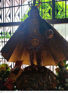 a statue of a baby jesus with a crown on his head is surrounded by flowers