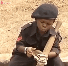 a young boy in a military uniform is sitting on the ground holding a stick and a bunch of money .