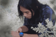 a man with long hair is wearing a watch with a blue dial