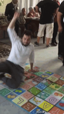 a man in a white shirt is kneeling on a colorful checkered mat with the letter l in the middle