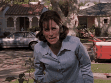 a woman in a blue shirt is standing in front of a house with a car parked in front of it