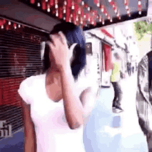 a woman is covering her face with her hand while walking down a street .