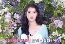 a woman stands in front of a wall of purple and white flowers with korean writing