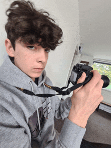 a young man wearing a grey nikon sweatshirt holds a camera