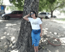 a woman leaning against a tree wearing a white gucci shirt