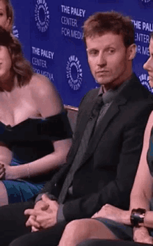 a man in a suit and tie sits in front of a wall that says the paley center for media