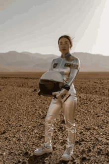 a woman in an astronaut costume holds a helmet in the desert