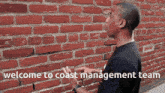 a man standing in front of a red brick wall with the words welcome to coast management team written on it