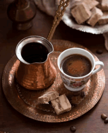 a cup of coffee sits on a copper tray next to a coffee pot