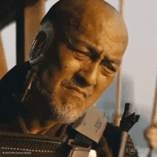 a bald man with a beard is holding a gun in a scene from the movie the creator .